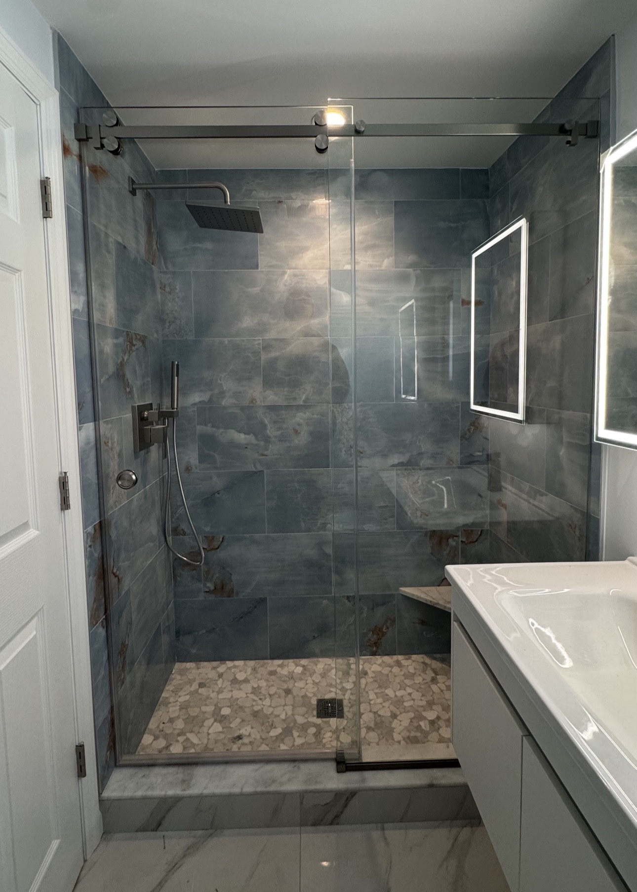 Frameless sliding shower door with a barn-style top rail and blue-gray tile